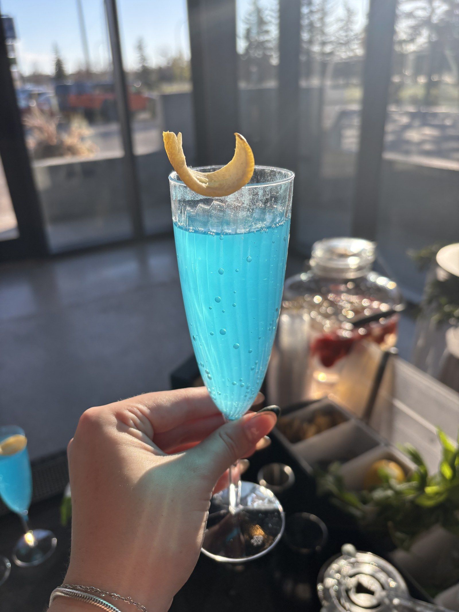 A bright blue sparkling drink in a flute with a curled lemon peel, in the afternoon sun