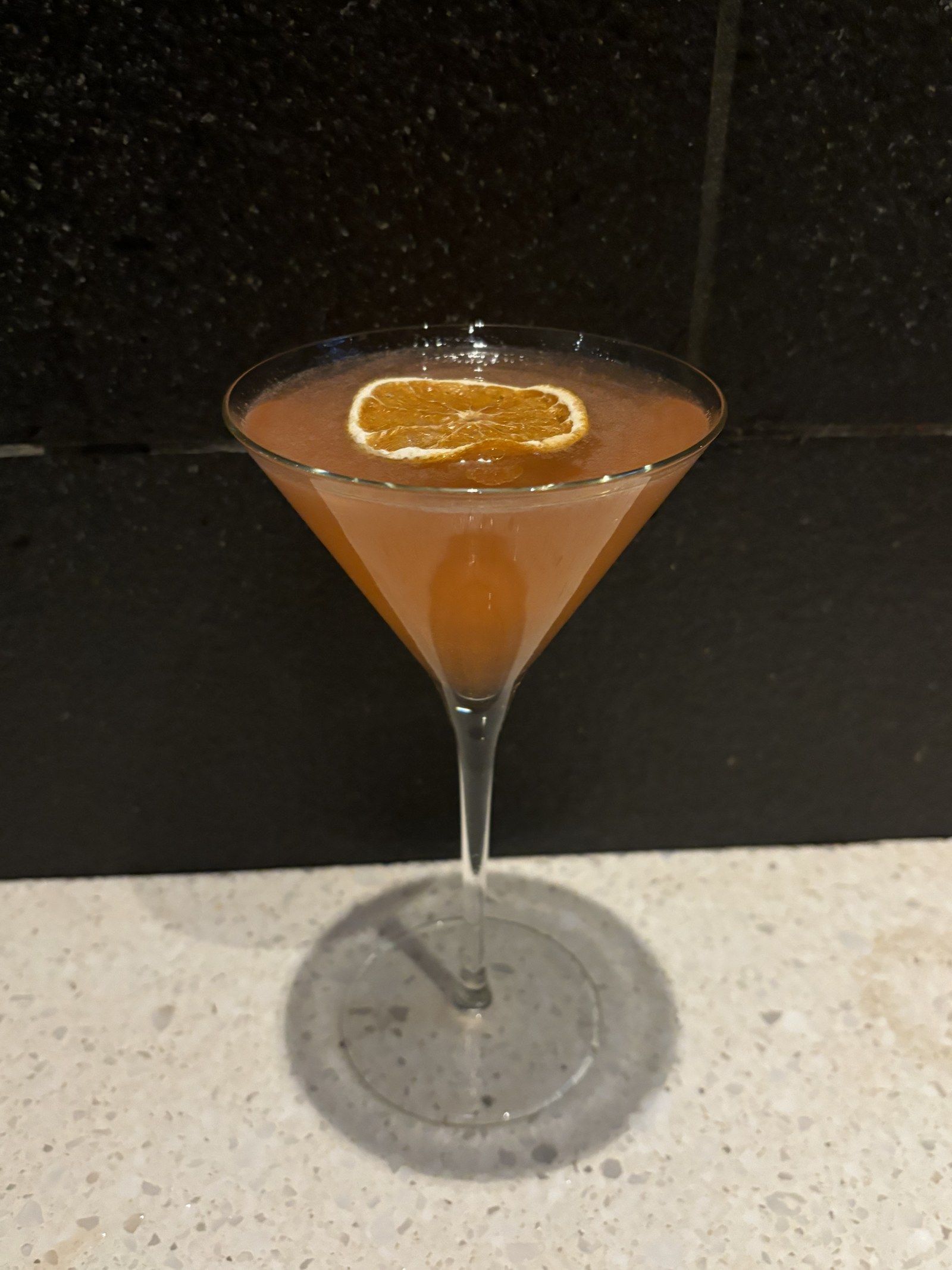 An orange martini with a dried orange wheel on a stone counter