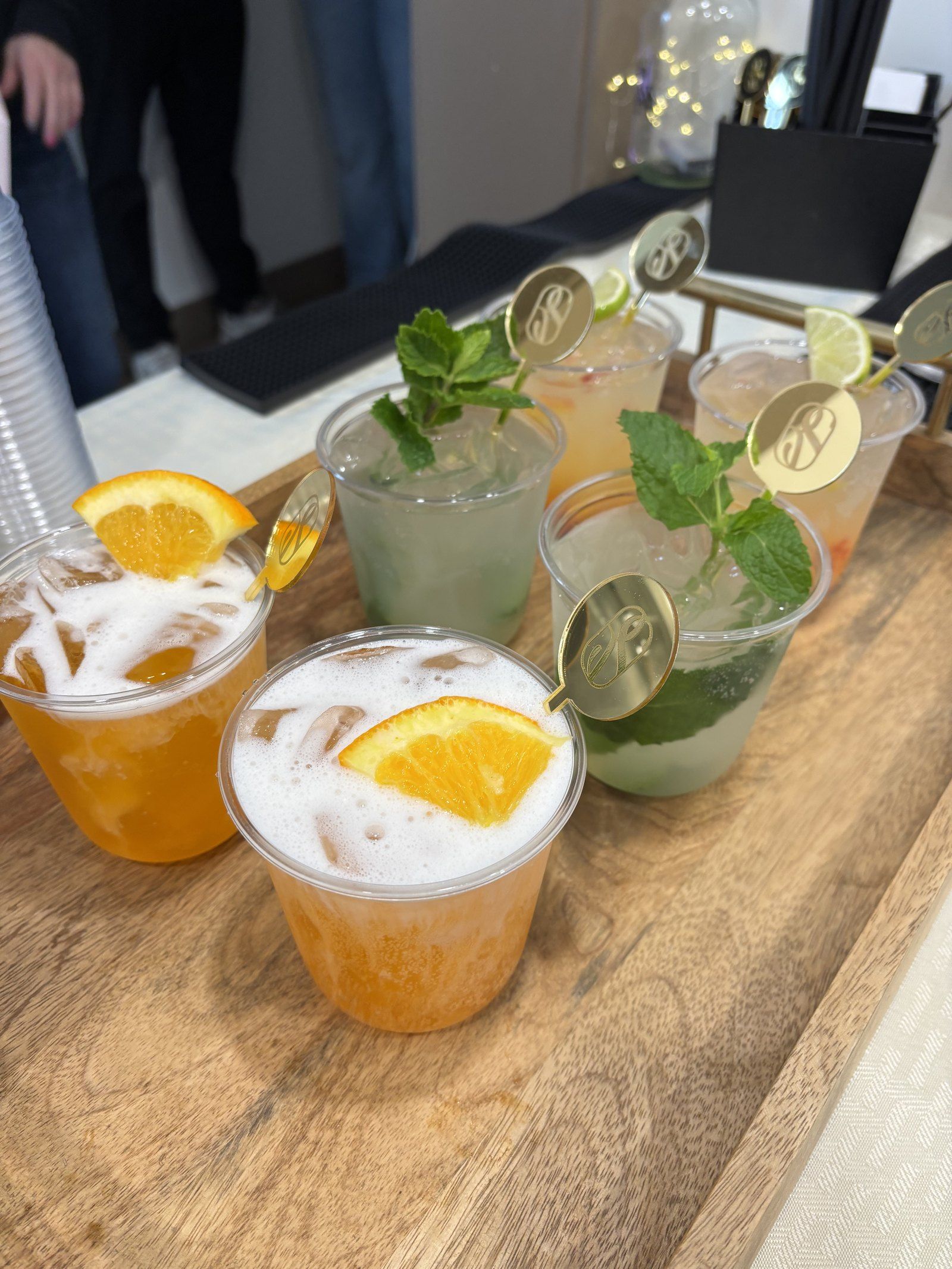A tray of cocktails with orange slices, mint and lime, each with a personalized gold drink stirrer
